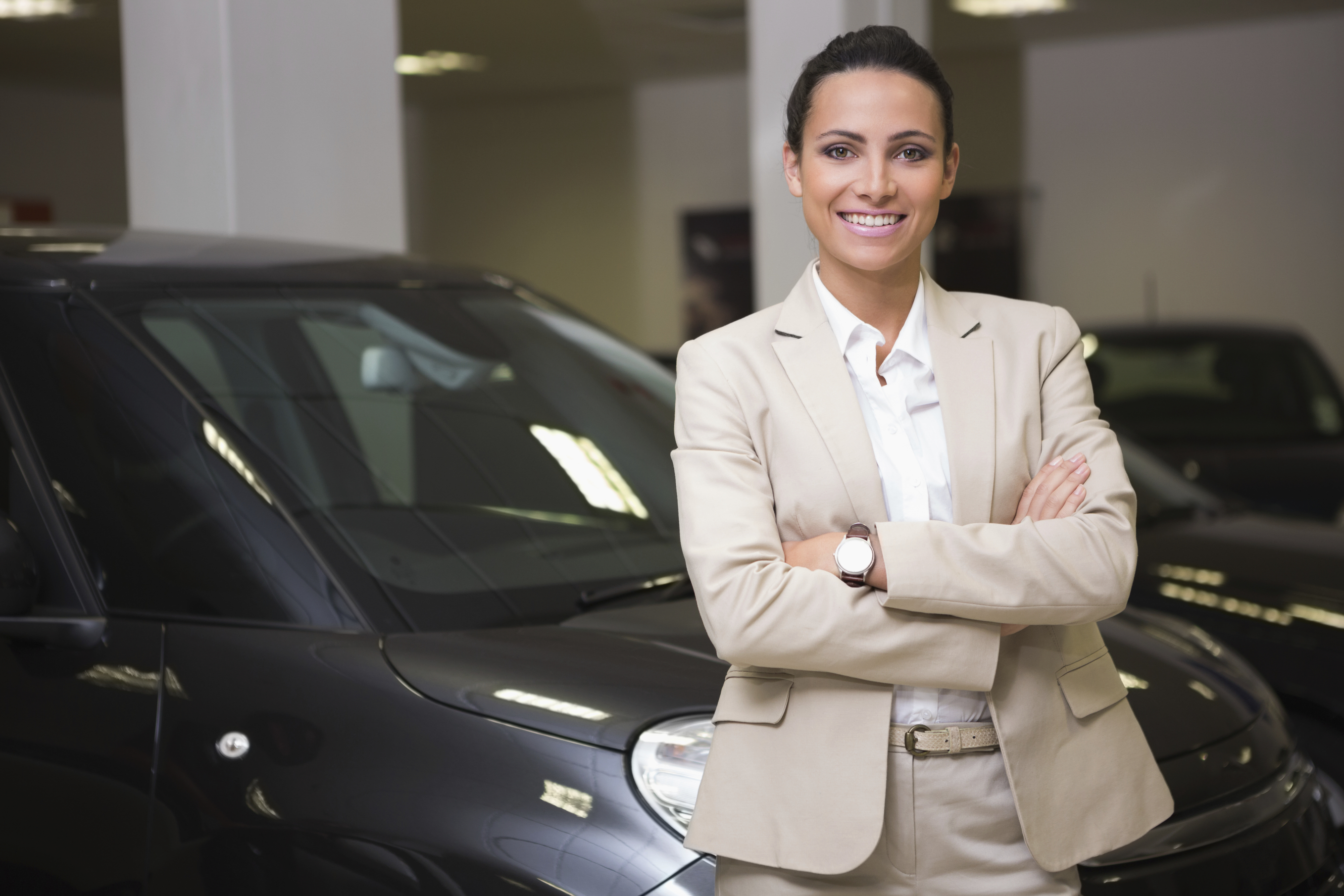 Smiling businesswoman standing with arms crossed at new car showroom