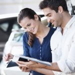 Positive couple smiling and browsing a catalogue in a car dealership