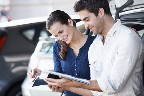 Positive couple smiling and browsing a catalogue in a car dealership